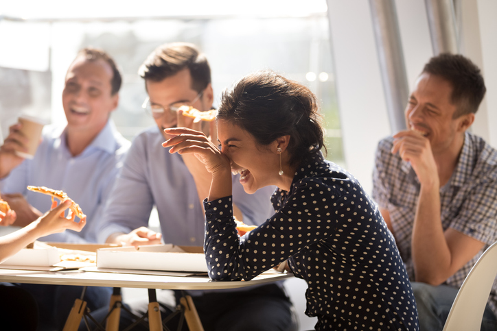 Indian woman laughing eating pizza with diverse coworkers in office