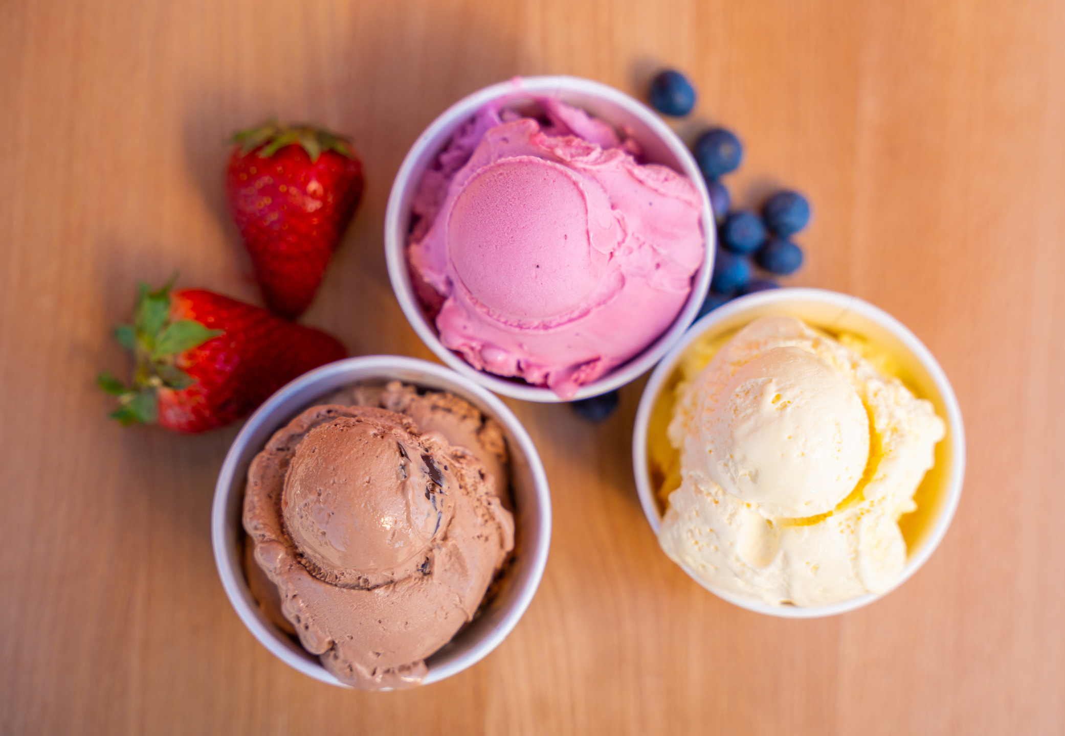 Colorful ice cream scoops in paper cups with berries on wooden table